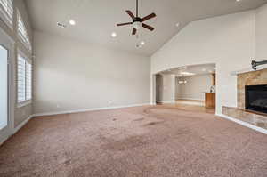 Spacious Great room featuring high vaulted ceiling, ceiling fan, fireplace, light colored carpet, patio and kitchen access