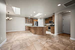 Kitchen featuring a skylight, appliances with stainless steel finishes, an island with sink, light tile patterned flooring, light marble counters and garage entrance