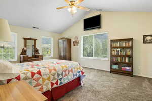 Carpeted bedroom with ceiling fan, lofted ceiling, and multiple windows