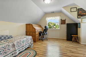 Bedroom with a textured ceiling, light wood-type flooring, and lofted ceiling