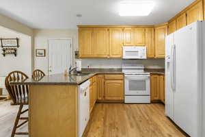 Kitchen with dark stone countertops, white appliances, sink, light hardwood / wood-style flooring, and kitchen peninsula