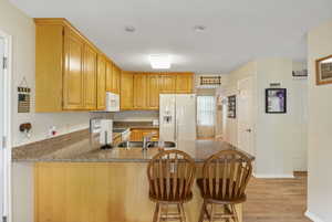 Kitchen featuring light hardwood / wood-style flooring, kitchen peninsula, dark stone countertops, white appliances, and sink