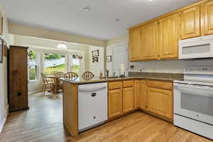 Kitchen with white appliances, light hardwood / wood-style flooring, sink, and kitchen peninsula