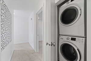 Laundry area with stacked washer / drying machine and light colored carpet