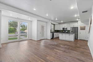 Kitchen with appliances with stainless steel finishes, a kitchen island, wood-type flooring, and white cabinetry