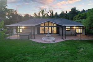 Back house at dusk featuring a lawn and a patio