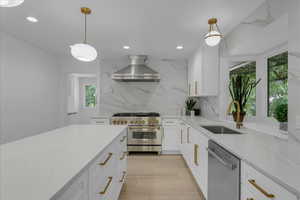 Kitchen featuring appliances with stainless steel finishes, light stone countertops, sink, tasteful backsplash, and wall chimney exhaust hood