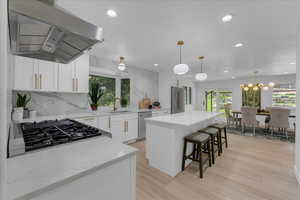 Kitchen featuring tasteful backsplash, white cabinets, range hood, and a kitchen island