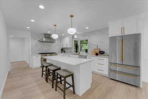 Kitchen featuring appliances with stainless steel finishes, tasteful backsplash, white cabinetry, a center island, and wall chimney range hood