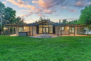 Back house at dusk featuring a pergola, a patio area, and a yard