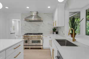 Kitchen featuring light stone countertops, backsplash, sink, range with two ovens, and wall chimney exhaust hood