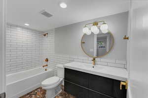 Full bathroom with tile walls, tiled shower / bath, toilet, tile patterned floors, and vanity