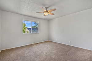 Carpeted empty room with ceiling fan and a textured ceiling