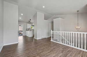 Empty room with a notable chandelier, vaulted ceiling, and dark hardwood / wood-style floors