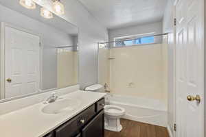 Full bathroom featuring a textured ceiling, toilet, hardwood / wood-style floors, washtub / shower combination, and vanity