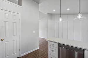 Bar featuring dark hardwood / wood-style floors, white cabinets, hanging light fixtures, light stone countertops, and stainless steel dishwasher