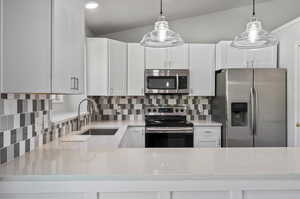 Kitchen featuring decorative backsplash, light stone counters, stainless steel appliances, and lofted ceiling