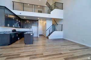 Kitchen featuring light stone countertops, a towering ceiling, light hardwood / wood-style flooring, and black / electric stove