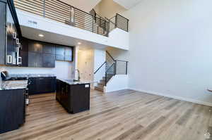 Kitchen featuring light stone counters, a towering ceiling, a center island with sink, light wood-type flooring, and sink