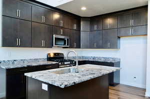 Kitchen featuring appliances with stainless steel finishes, light hardwood / wood-style floors, light stone counters, sink, and dark brown cabinetry