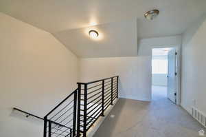 Staircase featuring a textured ceiling, carpet flooring, and vaulted ceiling