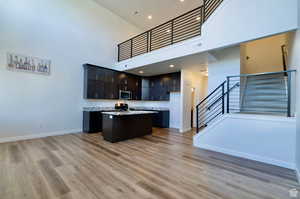 Kitchen with range, a kitchen island with sink, light hardwood / wood-style floors, and a towering ceiling