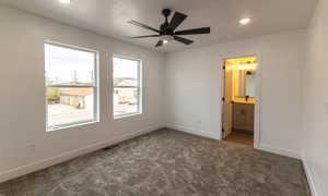Unfurnished bedroom with connected bathroom, ceiling fan, and dark carpet
