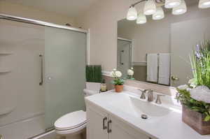 Bathroom with vanity, a shower with door, and toilet