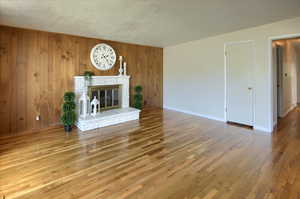 Unfurnished living room with hardwood / wood-style flooring, a textured ceiling, wooden walls, and a brick fireplace