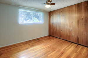 Spare room featuring ceiling fan, light wood-type flooring, a textured ceiling, and wooden walls