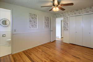 Unfurnished bedroom with ceiling fan, light wood-type flooring, ensuite bath, and a textured ceiling