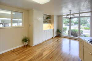 Interior space with an inviting chandelier, decorative light fixtures, white cabinets, and light hardwood / wood-style floors