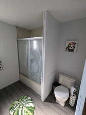 Bathroom featuring hardwood / wood-style floors, a shower with door, a textured ceiling, and toilet