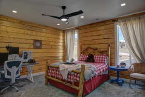Carpeted bedroom with wooden walls, a ceiling fan, and recessed lighting