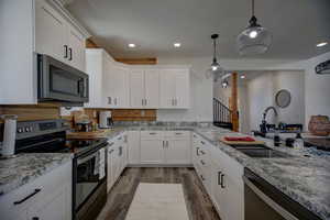 Kitchen with appliances with stainless steel finishes, dark wood-style flooring, white cabinetry, and pendant lighting