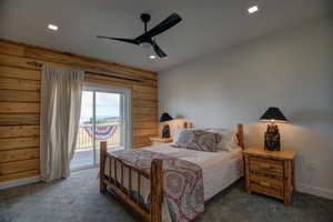 Bedroom with access to outside, wooden walls, carpet floors, and ceiling fan