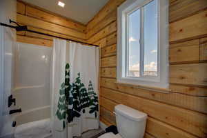 Full bath featuring wooden walls and shower / bath combo with shower curtain