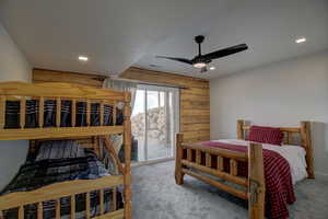 Bedroom featuring access to outside, wood walls, carpet, and a ceiling fan