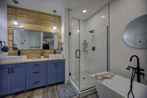 Full bathroom featuring a shower stall, a freestanding bath, double vanity, and wood finished floors