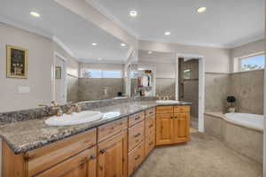 Bathroom with dual vanity, a relaxing tiled tub, a healthy amount of sunlight, and crown molding