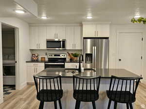 Kitchen with a textured ceiling, stainless steel appliances, a kitchen island with sink, light hardwood / wood-style floors, and sink