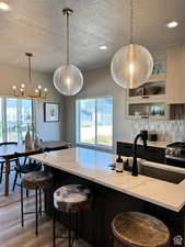 Kitchen featuring light wood-type flooring, tasteful backsplash, a kitchen breakfast bar, and decorative light fixtures