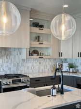 Kitchen with stainless steel gas stove, backsplash, light stone counters, and sink