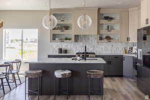 Kitchen with a kitchen island with sink, a breakfast bar area, decorative backsplash, light wood-type flooring, and decorative light fixtures