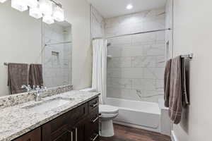 Guest house bathroom featuring hardwood / wood-style floors, shower / bath combo, vanity, and toilet