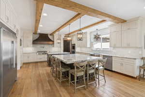 Kitchen featuring premium range hood, appliances with stainless steel finishes, backsplash, light hardwood / wood-style flooring, and beamed ceiling