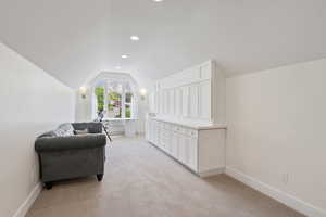 Living area in bedroom with lofted ceiling and light colored carpet