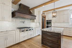 Kitchen featuring custom exhaust hood, decorative light fixtures, stainless steel appliances, and light hardwood / wood-style floors