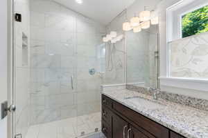 Guest house bathroom featuring a shower with shower door, vanity, and vaulted ceiling