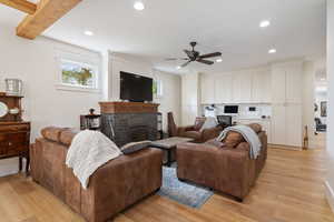 Living room with beam ceiling, a healthy amount of sunlight, light hardwood / wood-style floors, and a brick fireplace